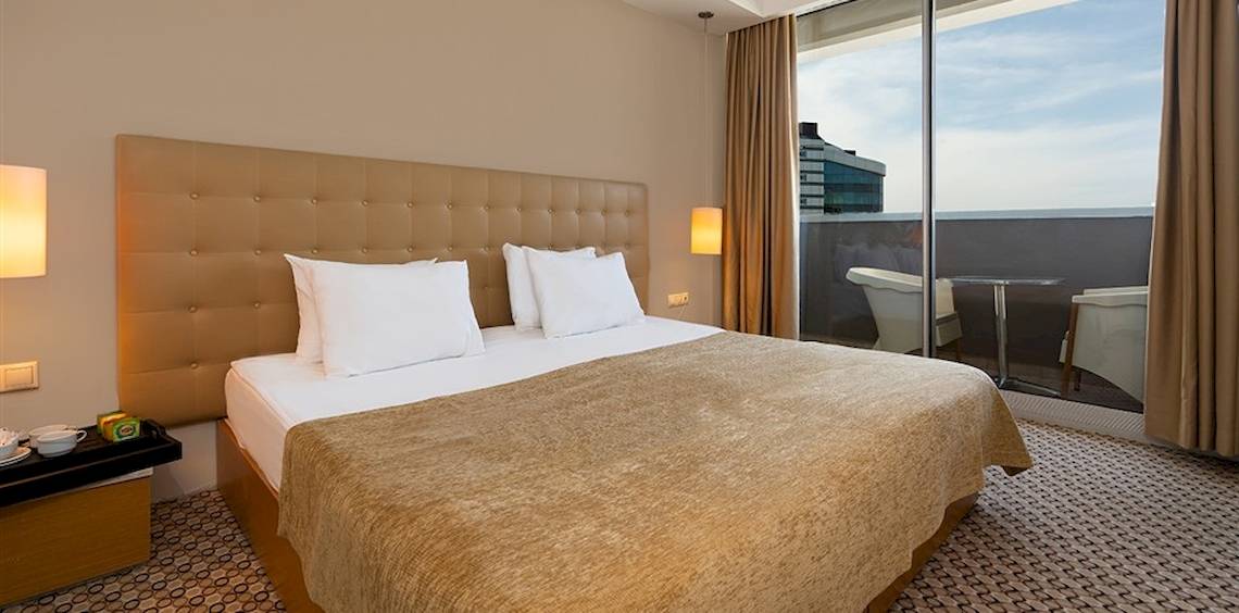 Ein Hotelzimmer im Crystal Centro Resort mit einem großen Bett, einem Balkon und Blick auf die Stadt.