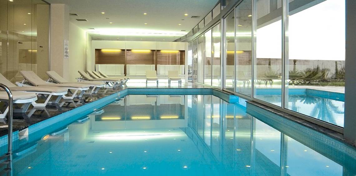 Innenpool im Crystal Centro Resort mit weißen Liegen und großen Glaswänden.