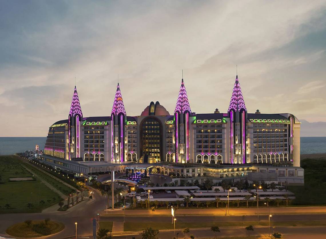 Das Delphin Imperial Hotel in der Abendbeleuchtung mit violetten Lichtern und Meer im Hintergrund.
