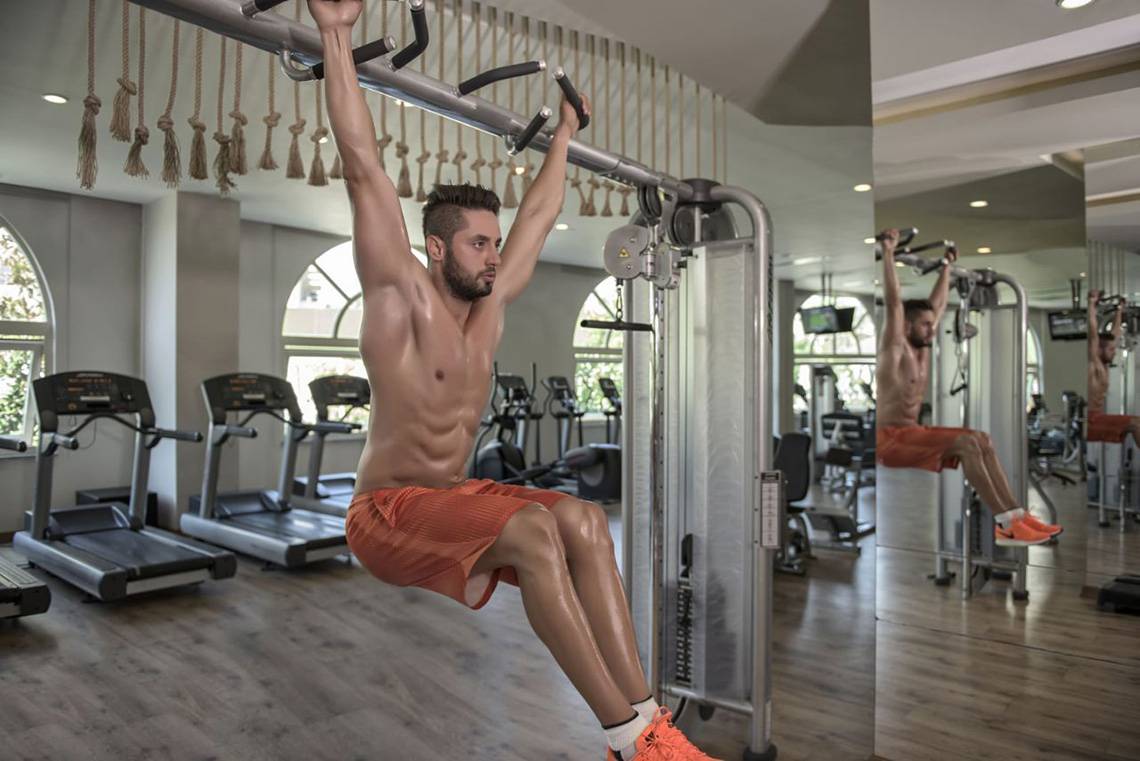 Ein Mann trainiert im Fitnessstudio des Delphin Imperial Hotels mit Klimmzugstangen.