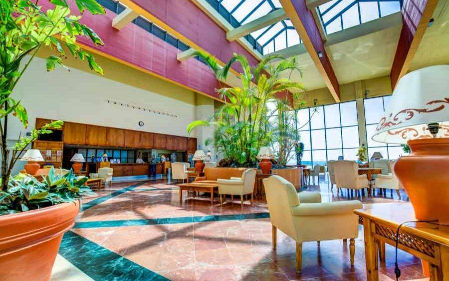 Lobby des SBH Club Paraiso Playa Hotels mit großen Pflanzen und Möbeln.