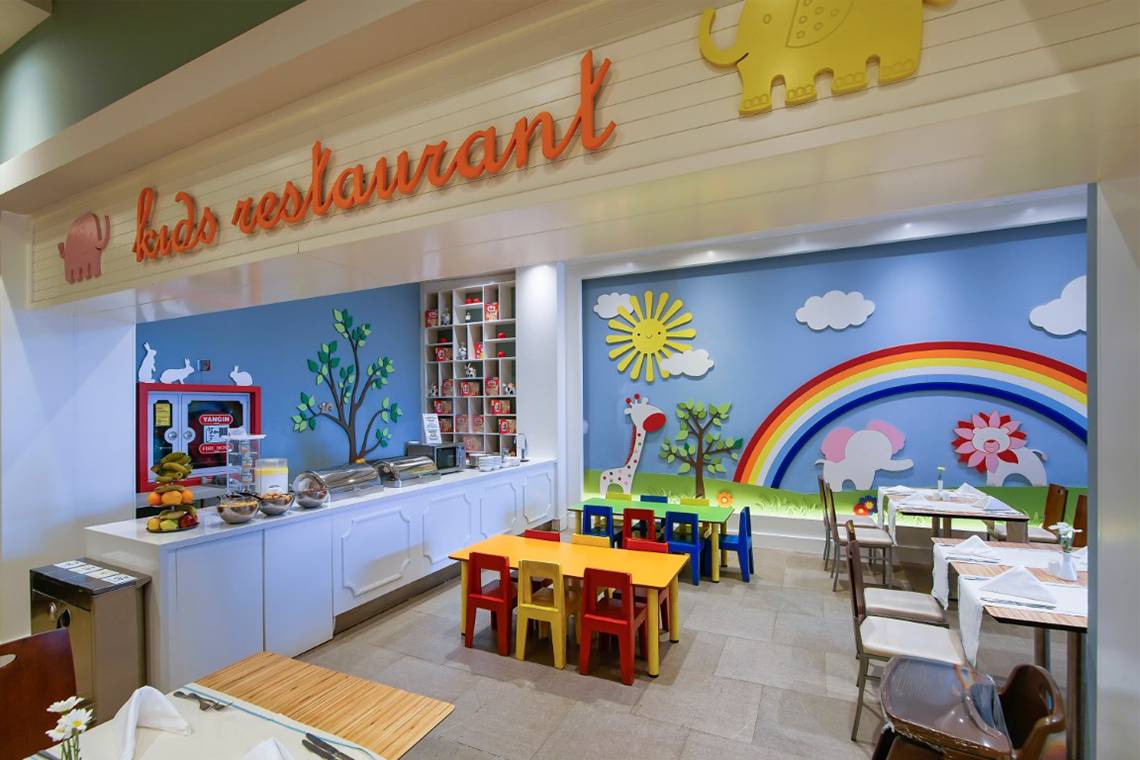 Kinderrestaurant im Limak Lara De Luxe Hotel & Resort mit bunten Wandmalereien und farbenfrohen Tischen und Stühlen.