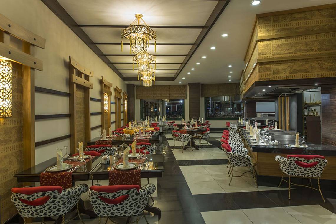 Innenansicht des Restaurants Delphin Palace mit gedeckten Tischen und Stühlen, dekorativen Kronleuchtern und Wandleuchten.