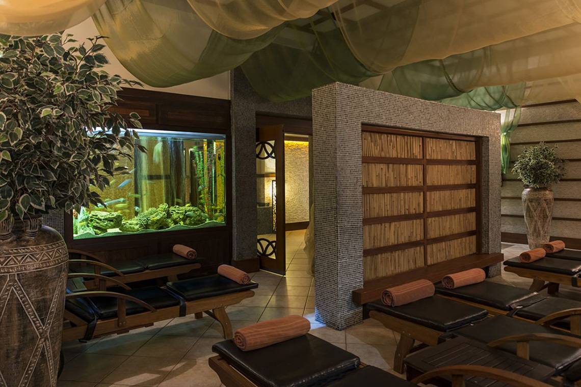 Spa-Lounge-Bereich im Delphin Palace Hotel mit Lounge-Liegestühlen und einem großen Aquarium.