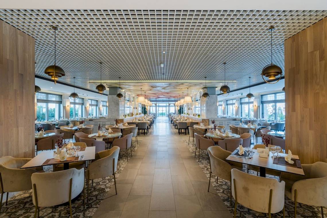 Innenansicht des Restaurants im Fame Residence Kemer & Spa Hotel mit gedeckten Tischen und hängenden Lampen.