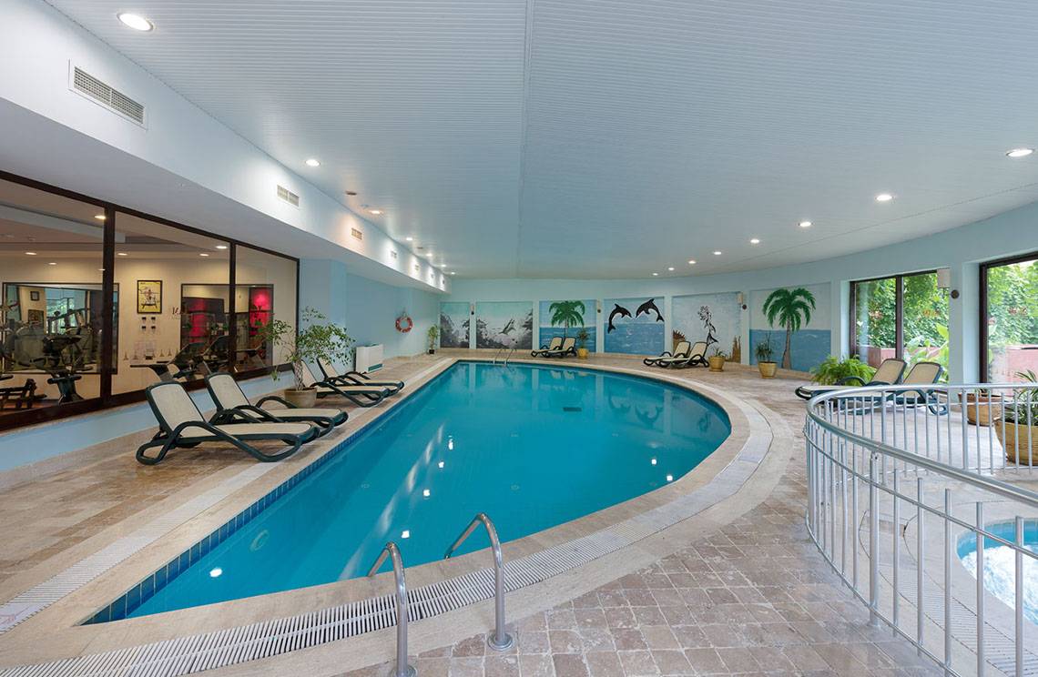 Innenpool im Siam Elegance Hotels & Spa mit Loungeliegen und tropischen Wandmalereien.