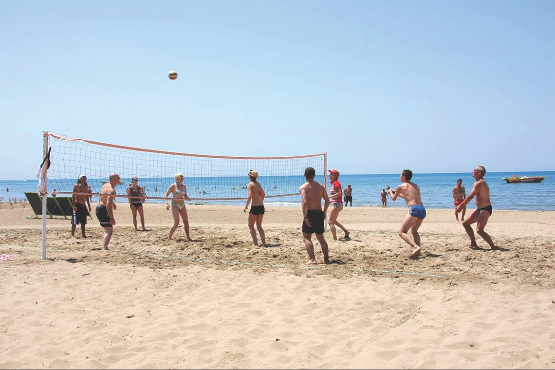 Gruppe von Menschen spielt Volleyball am Strand, im Hintergrund ist das Meer zu sehen.