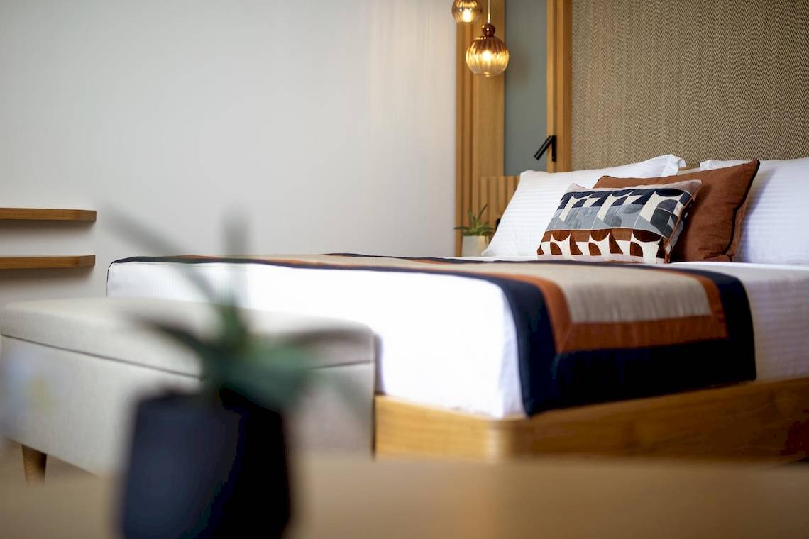 Schlafzimmer im Lyttos Mare Hotel mit Doppelbett, Kissen, Nachttisch und Beleuchtung.