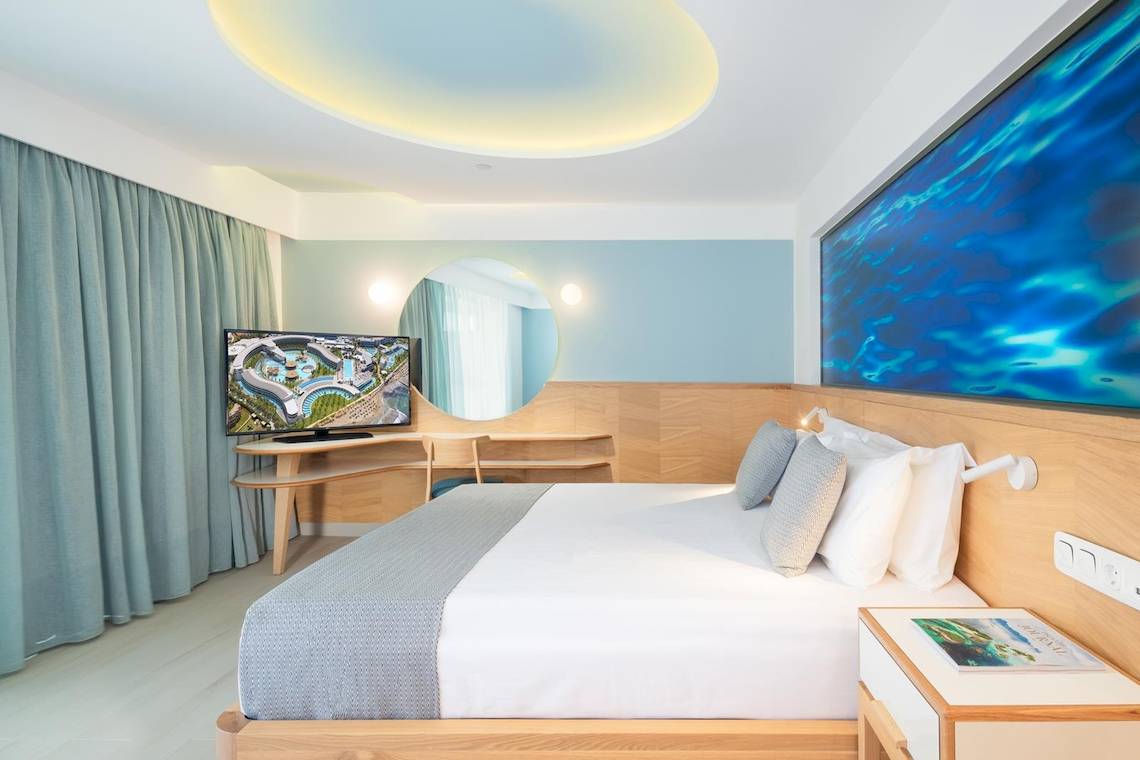 Innenansicht eines Zimmers im Lyttos Mare Hotel mit einem Bett, Fernseher und Deko.