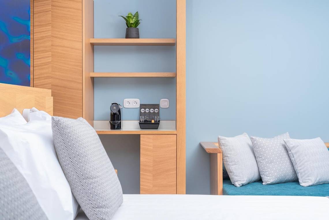 Innenansicht eines Hotelzimmers im Lyttos Mare Hotel mit einem Bett, Kissen, Schreibtisch und Pflanzen.