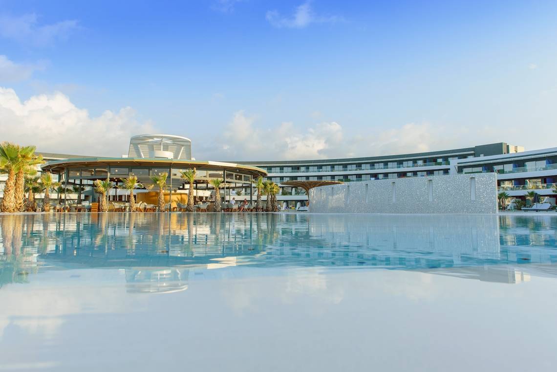 Außenpool des Lyttos Mare Hotels mit moderner Architektur und Palmen im Vordergrund.