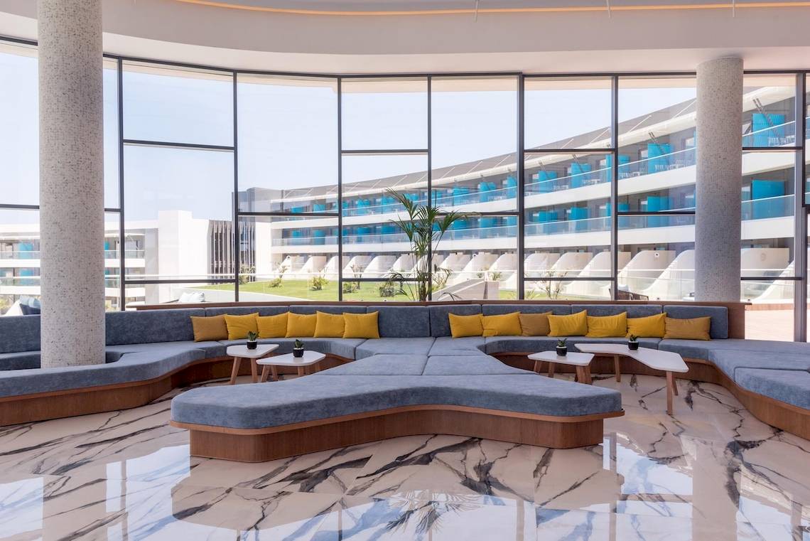 Innenansicht der Lobby im Lyttos Mare Hotel mit geschwungenen Sofas, runden Tischen und großen Fenstern.