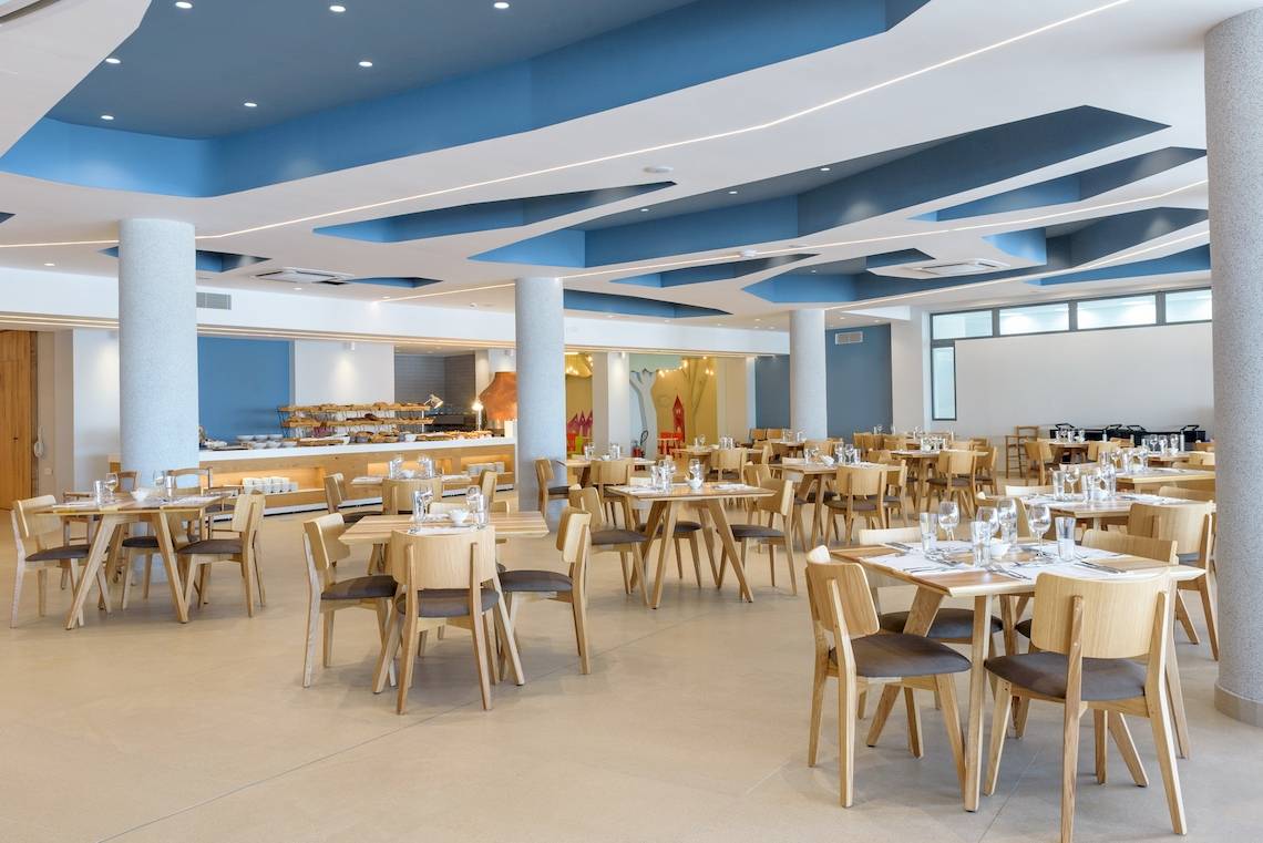 Innenansicht des Restaurants des Lyttos Mare Hotels mit blauen Decken und Holztischen.