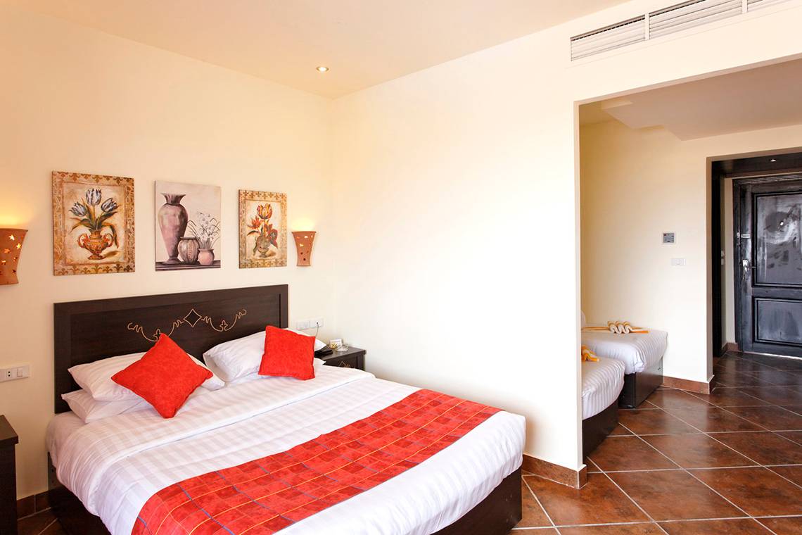 Schlafzimmer im Three Corners Sea Beach Resort mit zwei Betten, roten Kissen und dekorativen Gemälden an der Wand.