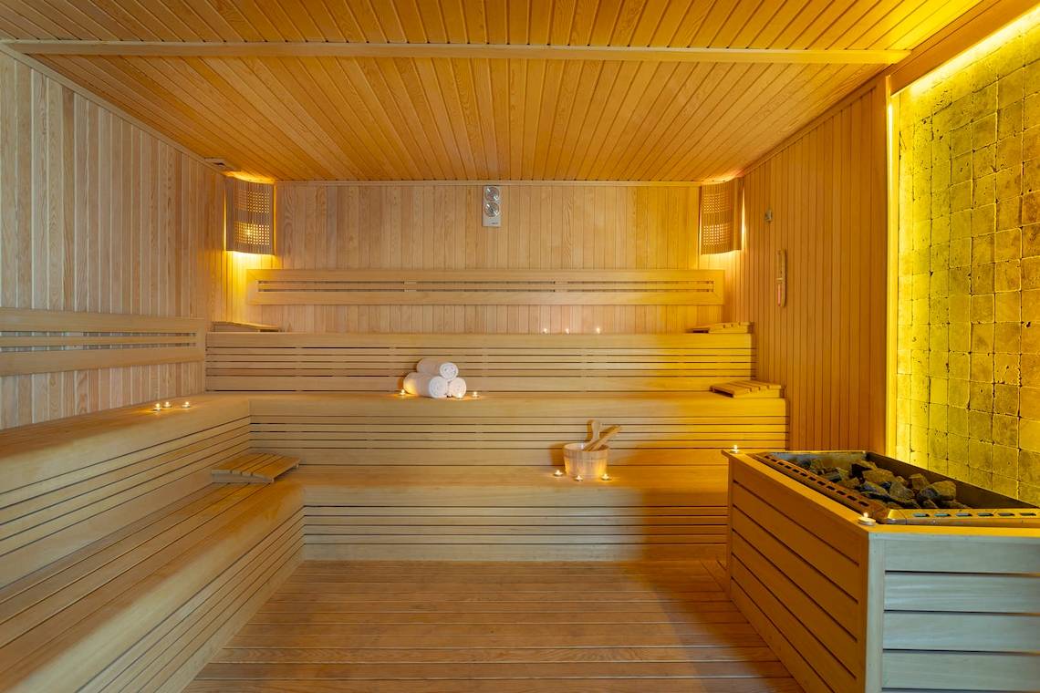Innenansicht einer Sauna im Duja Bodrum Hotel mit Holzbänken, gestapelten Handtüchern und einer gelben Wand.