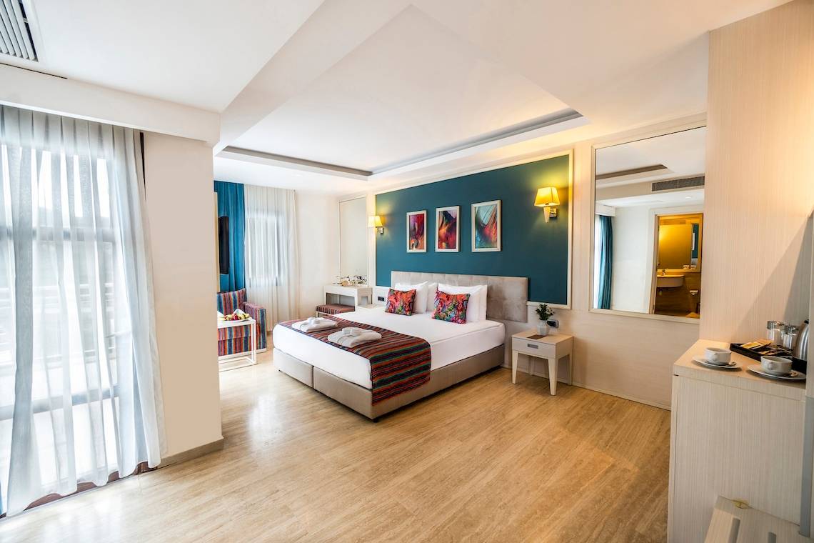 Schlafzimmer im Duja Bodrum Hotel mit Doppelbett, blauer Wand und Kunstwerken.