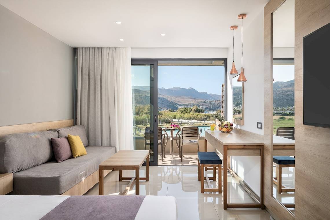 Innenansicht eines Zimmers im CHC Galini Palace Hotel mit Blick auf eine Terrasse und Berge.
