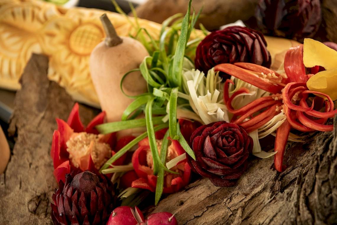 Nahaufnahme von Gemüse und Blumen auf Baumrinde, darunter Kürbis, Rosen und Paprika.