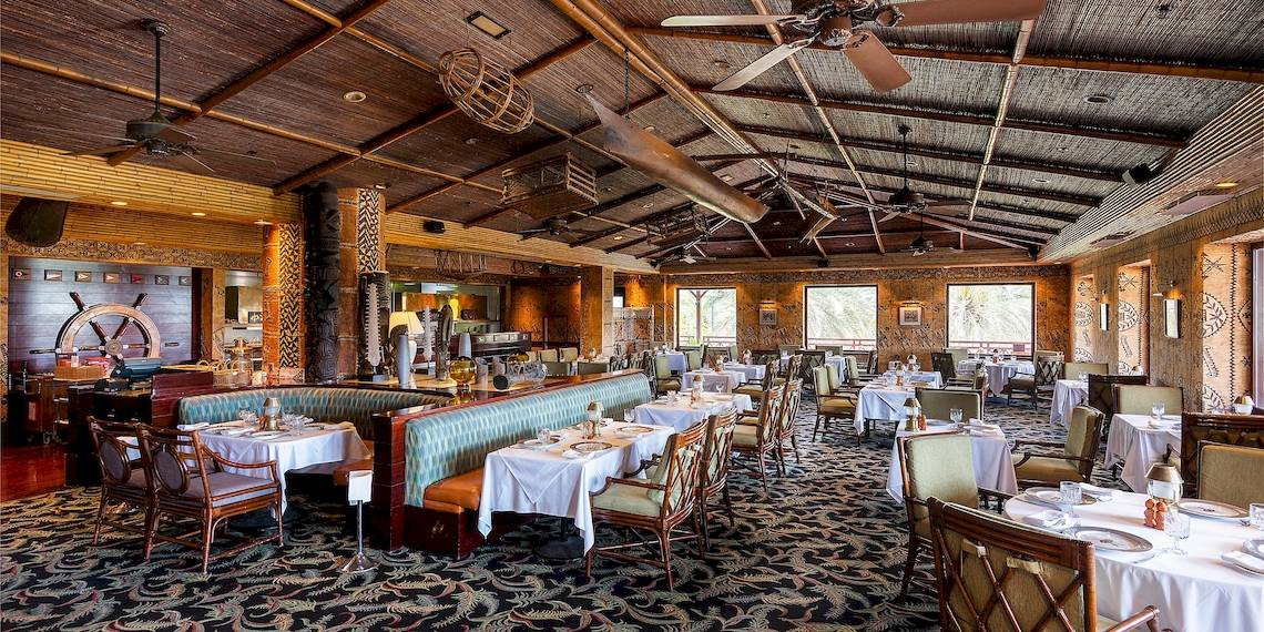 Innenbereich des Restaurants im InterContinental Muscat mit tropischen Dekor, Deckenventilatoren und runden Tischen.