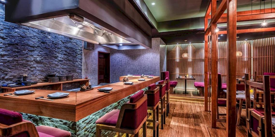 Innenraum des Sushi-Restaurants im InterContinental Muscat mit hölzerner Theke und roten Stühlen.