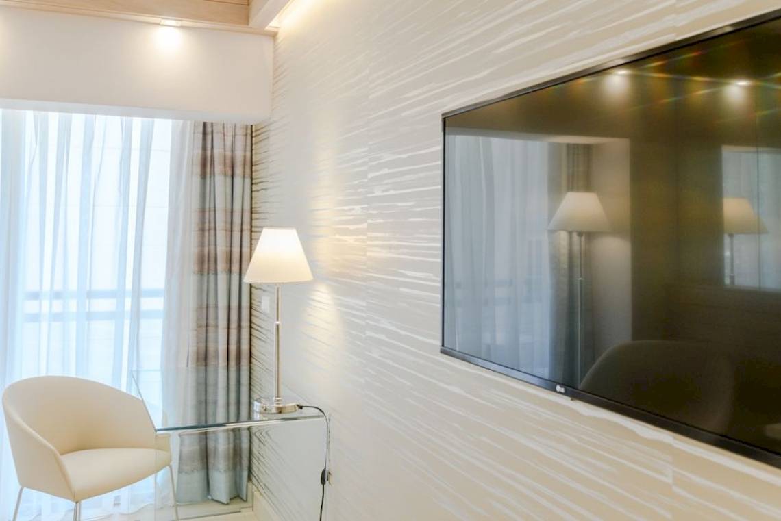 Zimmer im Mediterranean Hotel auf Rhodos mit Fernseher, Lampe und Sessel.