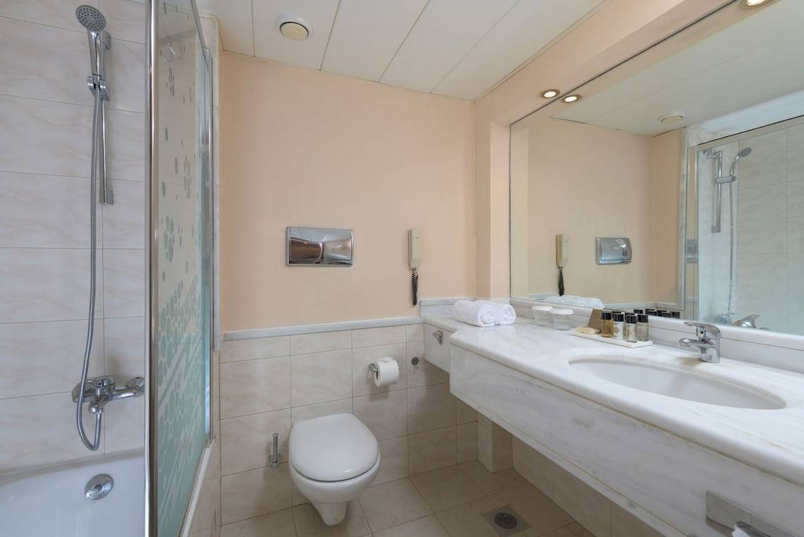 Badezimmer im Mediterranean Hotel auf Rhodos mit Badewanne, Dusche, Toilette, Waschbecken und Spiegel.