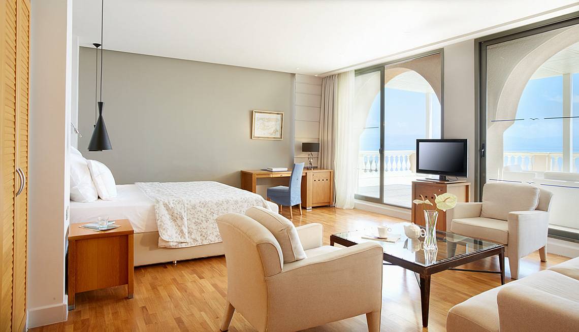 Innenansicht einer Hotelsuite im MarBella Corfu mit Bett, Schreibtisch und Fernseher auf dem Balkon.