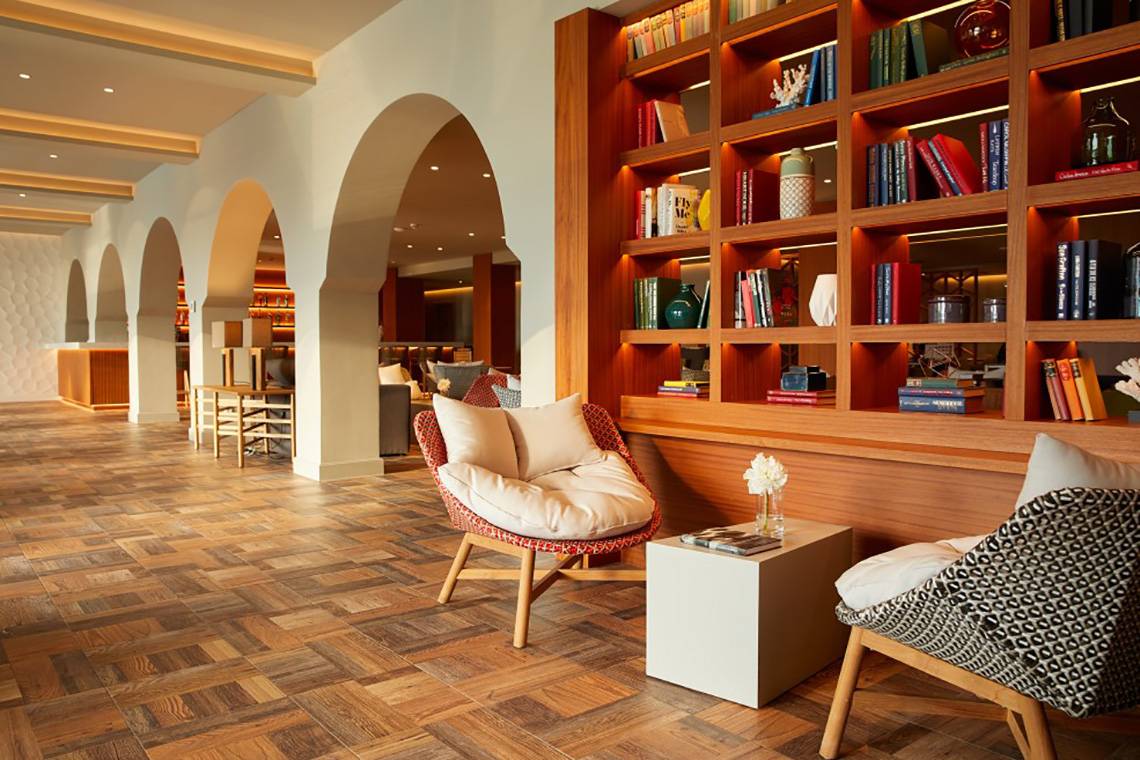 Loungebereich des MarBella Corfu Hotels mit Holzboden, runden Sesseln und Regalen voller Bücher.