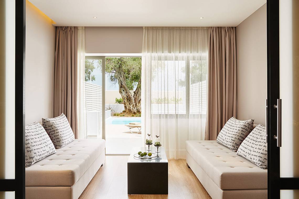 Innenansicht des Wohnzimmers im MarBella Corfu Hotel mit Möbeln und Ausblick auf den Pool.
