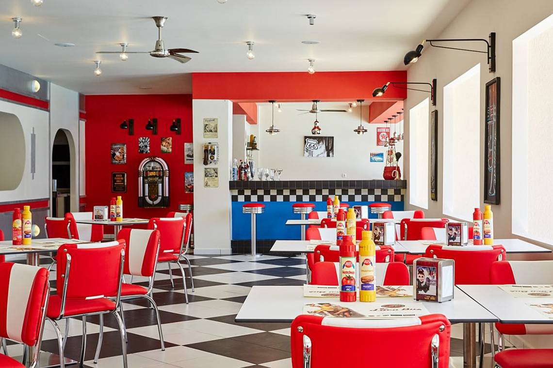 Innenraum des Restaurants im MarBella Corfu Hotel mit rotem und weißem Thema, schwarzen Fliesen und rot-weißen Stühlen.