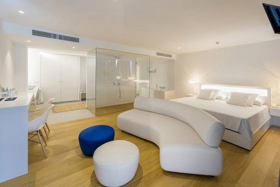 Innenansicht eines Zimmers im Vibra Algarb Hotel mit weißem Bett, Couch, blauem Hocker und weißem Schreibtisch.