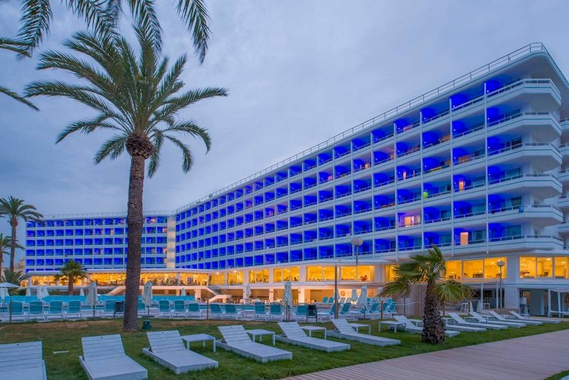 Außenansicht des Vibra Algarb Hotels mit blau beleuchteten Fenstern und Loungestühlen im Freien.