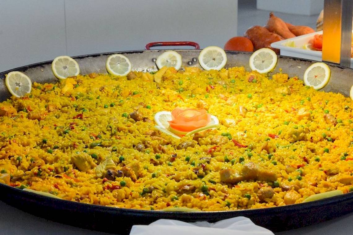 Großer Teller mit Paella, gefüllt mit Reis, Gemüse und Fleisch, dekoriert mit Zitronenscheiben.
