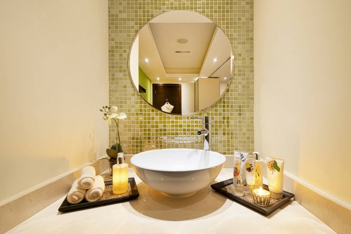 Badezimmer im Khalidiya Palace Rayhaan by Rotana mit grünen Fliesen, weißem Waschbecken und Kerzen.
