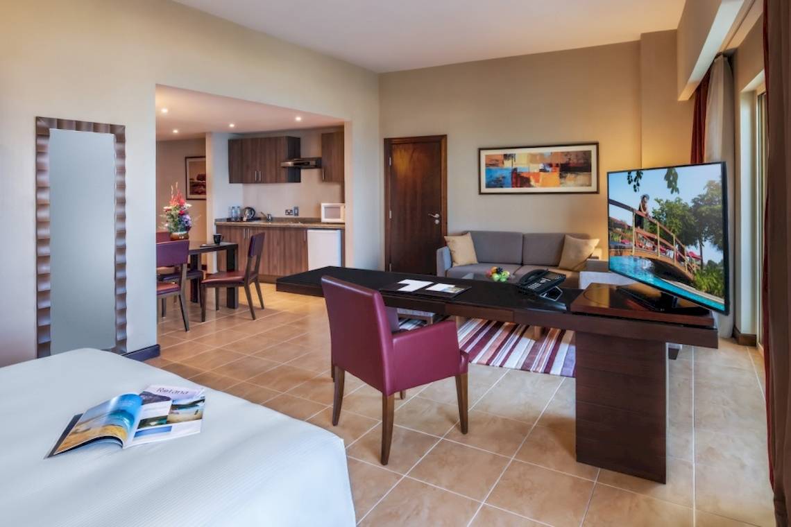 Innenansicht der Suite im Khalidiya Palace Rayhaan by Rotana Hotel mit Schreibtisch, Stuhl und Fernseher.
