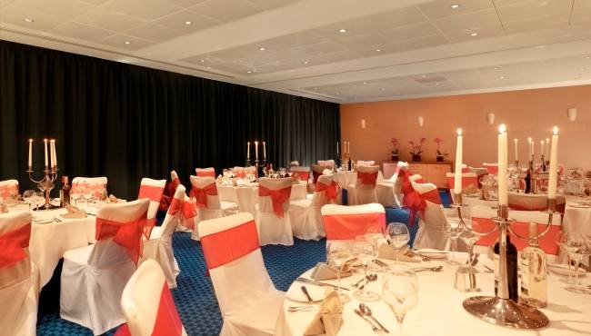 Bankettsaal im Park Plaza County Hall London mit gedeckten Tischen, Kerzen und roten Schleifen.