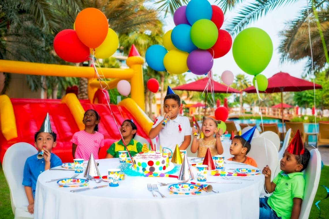 Kinder feiern einen Geburtstag im Khalidiya Palace Rayhaan by Rotana mit einer bunten Geburtstagstorte, Luftballons und einem aufblasbaren Schloss.