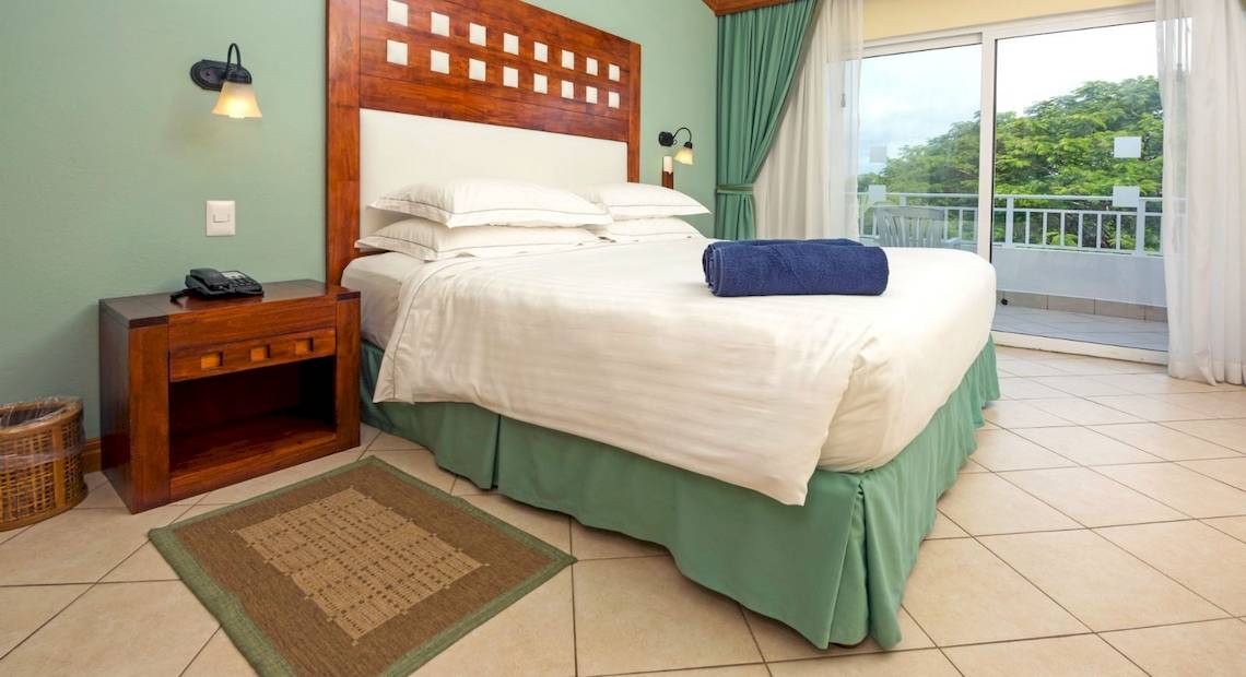 Doppelzimmer im Occidental Tamarindo Hotel mit Balkon und Blick auf Bäume.