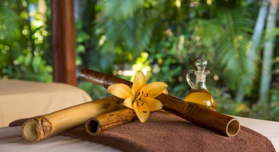 Bambusrohre, eine gelbe Blume und ein Ölflakon auf einem Massagebett im Freien.