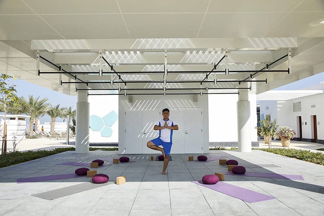 Ein Mann praktiziert Yoga auf einer Terrasse im Riu Dubai, umgeben von Yogamatten und Meditationskissen.