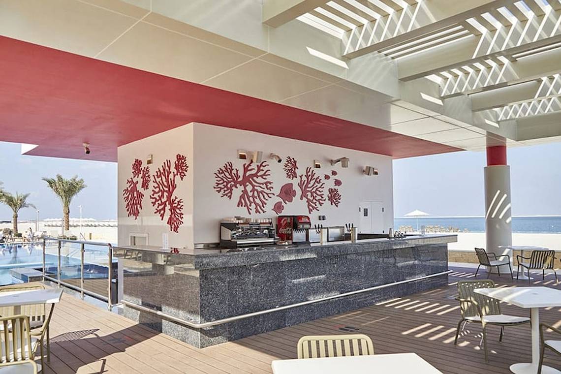 Terrassenbar des Riu Dubai Hotels mit Blick auf das Meer und rote Korallenmalereien an der Wand.