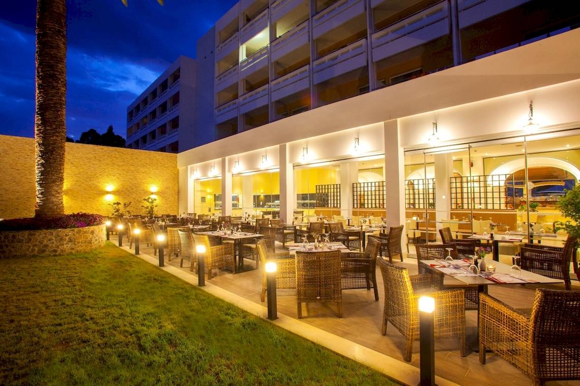 Außenbereich des Louis Kerkyra Blue Hotels bei Nacht mit beleuchteten Tischen und Stühlen.