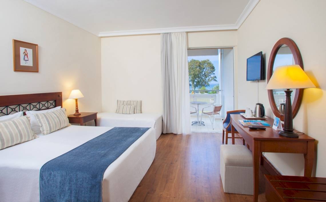 Innenansicht eines Hotelzimmers des Louis Kerkyra Blue mit zwei Betten, Schreibtisch, Lampen und Fernseher.
