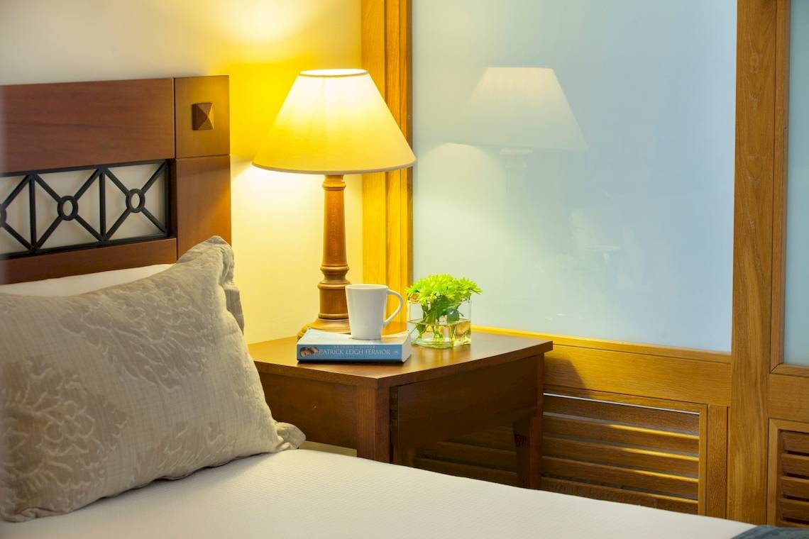 Bett im Zimmer im Louis Kerkyra Blue Hotel mit Kissen, Nachttisch und Lampe.