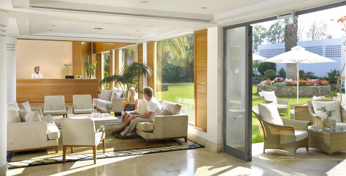 Zwei Personen sitzen in der Lounge des Louis Kerkyra Blue Hotels mit Blick auf eine Gartenterrasse.