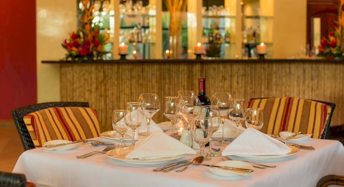 Ein gedeckter Tisch im Occidental Tamarindo Hotel mit Flasche, Gläsern und Besteck.