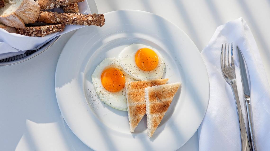Frühstück mit zwei Spiegeleiern, Toast und Brot auf einem weißen Teller.