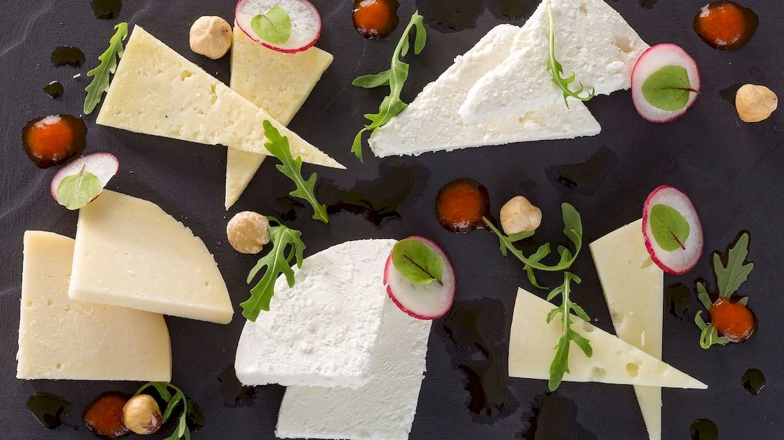 Verschiedene Käsesorten auf einem schwarzen Teller serviert, mit Radieschen, Rucola und Haselnüssen garniert, DeLight Boutique Hotel