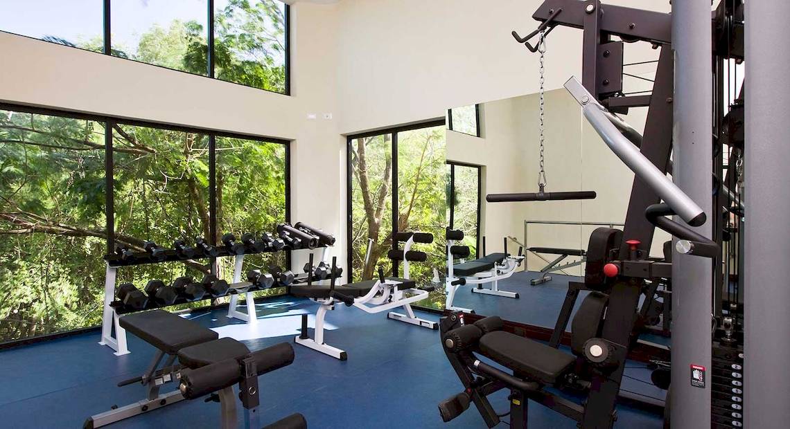 Fitnessraum im Occidental Tamarindo Hotel mit großen Fenstern und Blick auf Bäume.
