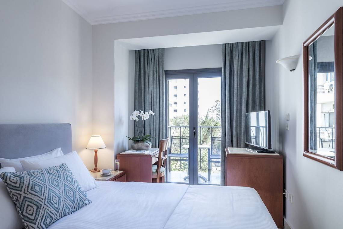 Innenansicht eines Hotelzimmers im Mitsis La Vita Beach Hotel mit Bett, Schreibtisch und Balkon